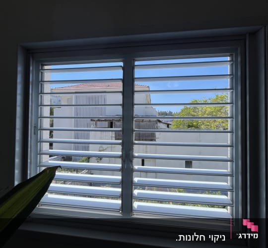 חלון עם תריסים ונוף חיצוני של בית ועצים